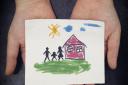 Child holds a drawn house with family adoption generic